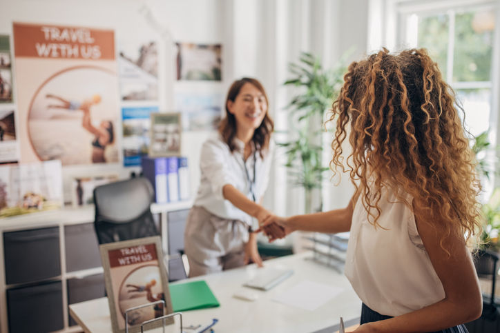 Two people, beautiful woman arriving in modern travel agency and shaking hands with travel agent.