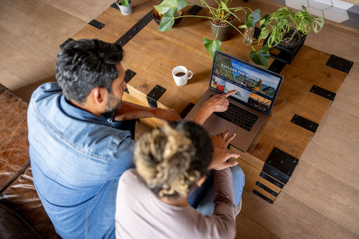 Happy couple at home booking a trip online using their laptop computer. **DESIGN ON SCREEN WAS MADE FROM SCRATCH BY US**