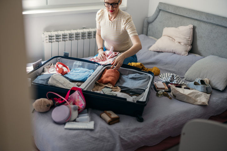 High angle view of a beautiful woman sitting on a bed and packing luggage for a family vacation.