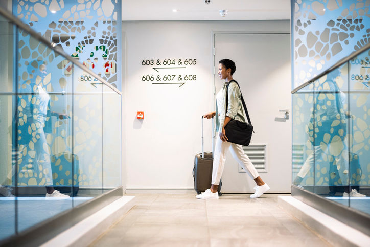 Young woman walking with wheeled luggage in hotel corridor