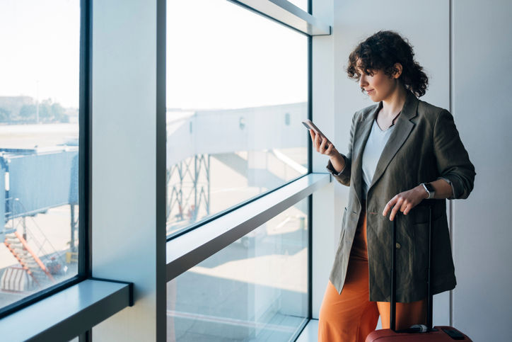 An elegant businesswoman waiting to board on a plane. She is checking necessary information about the flight using an app on her mobile phone. She looks happy about the trip.