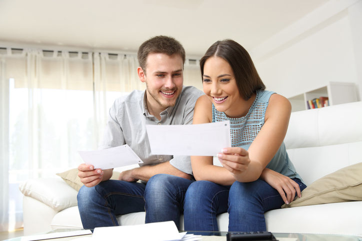 Happy young couple looking and checking bills on a couch at home