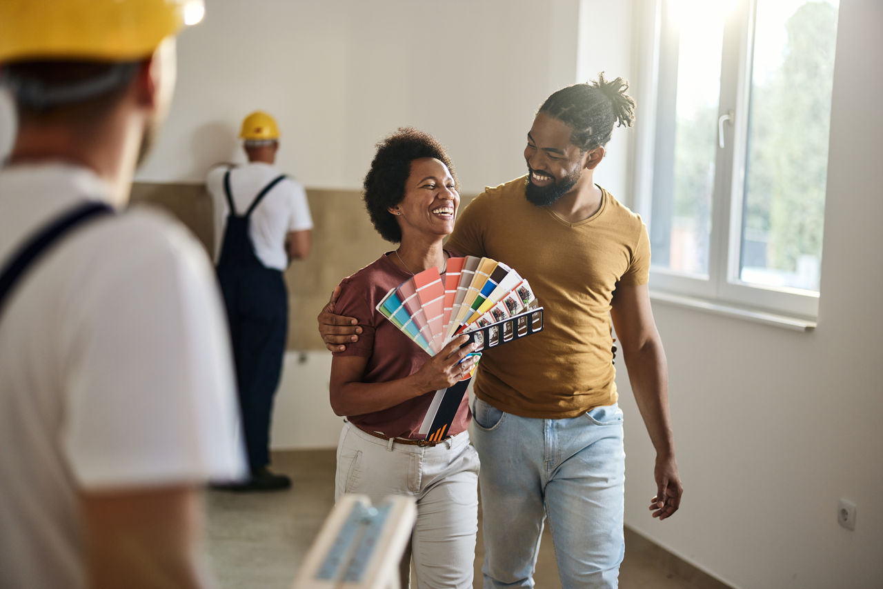 Happy African American couple enjoying while choosing colors for their new apartment with painters in it.