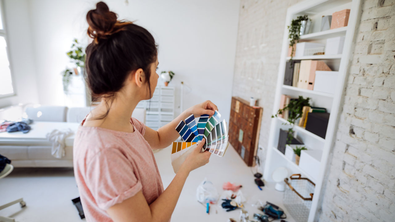 Young woman during reconstruction of apartment, holding color chart and choosing the right color for the wall