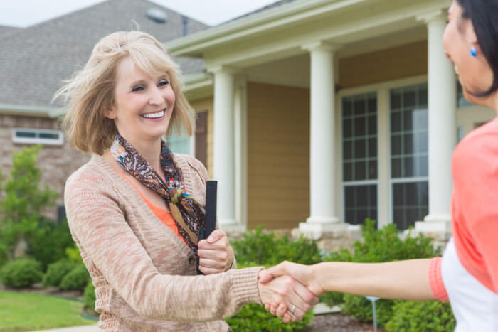 two middle aged women shaking hands outside of home