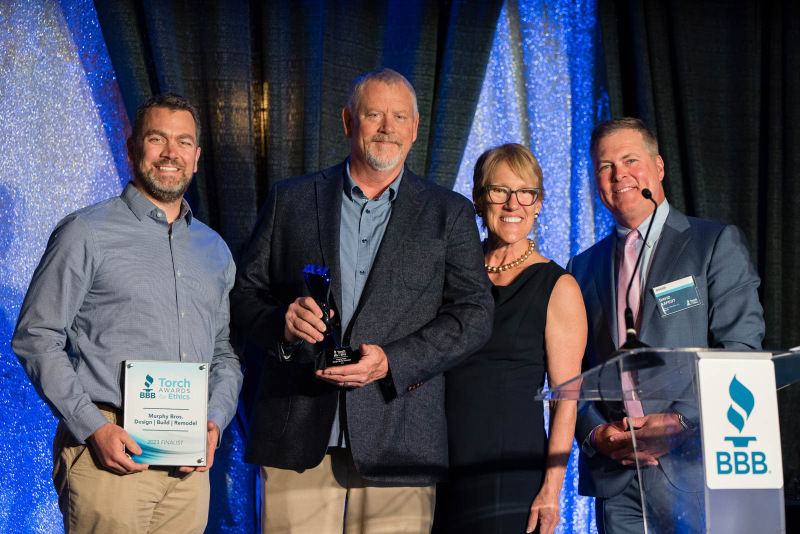 Owners of Murphy Bros pose on stage with BBB execs for a photo with their 2023 Torch Awards for Ethics trophy