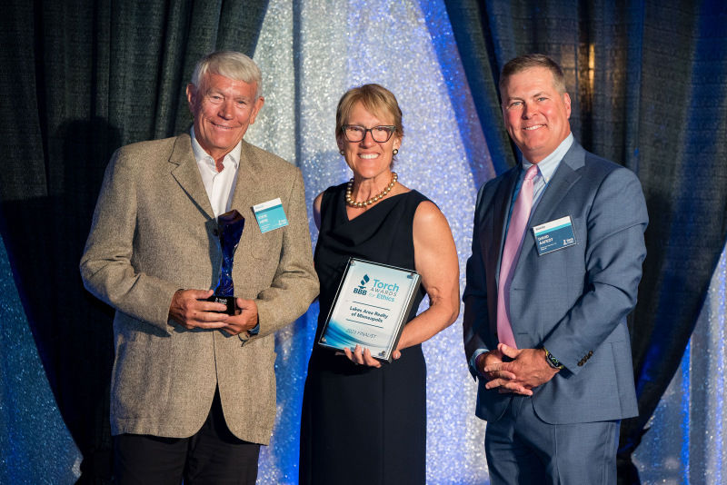 Owner of Lakes Area Realty of Mpls poses on stage with BBB execs for a photo with their 2023 Torch Awards for Ethics trophy