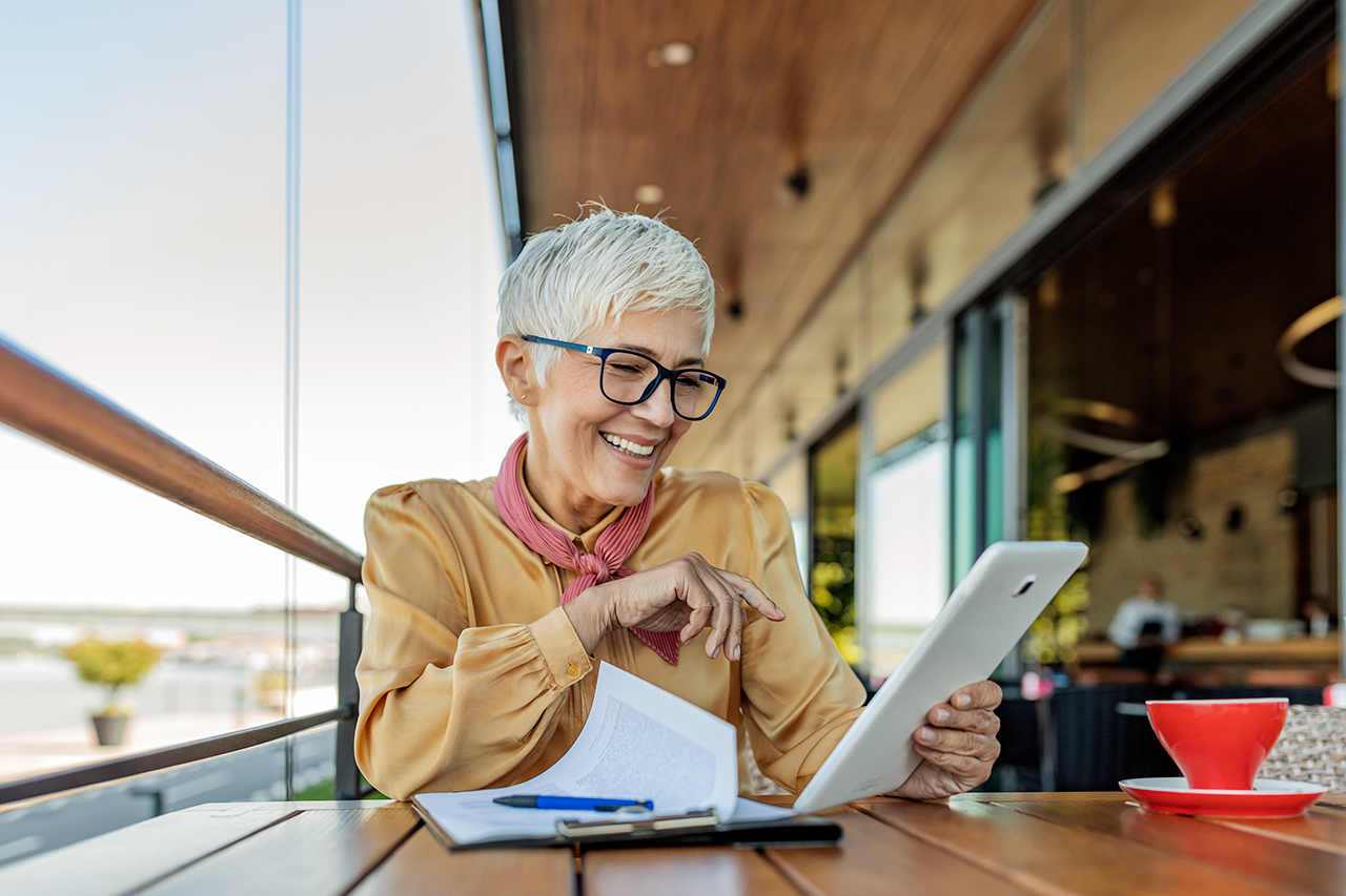Mature business woman at cafe using Tablet. Senior woman wearing eyeglasses reading on digital tablet. Female at cafe using digital tablet.