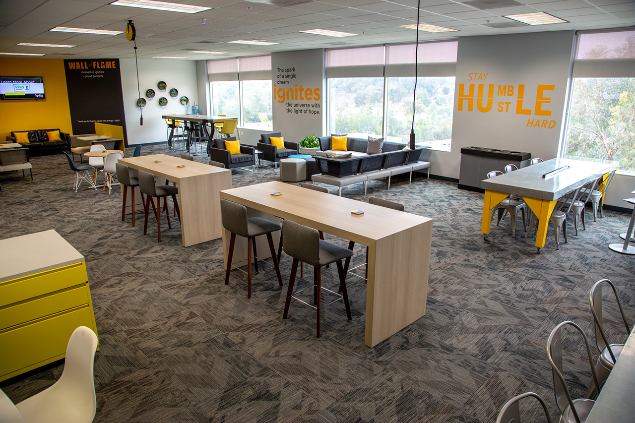 large room with modern furniture including tables, chairs, and cabinets, large windows looking out into a wooded area