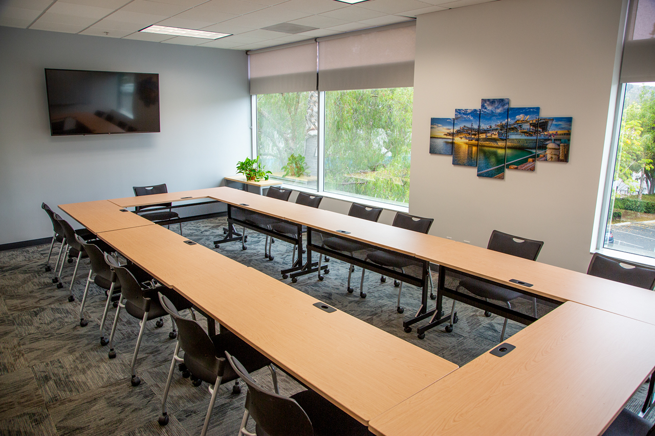 long conference table set up in a hollow rectangle with large windows looking out into the street and a large tv on the wall