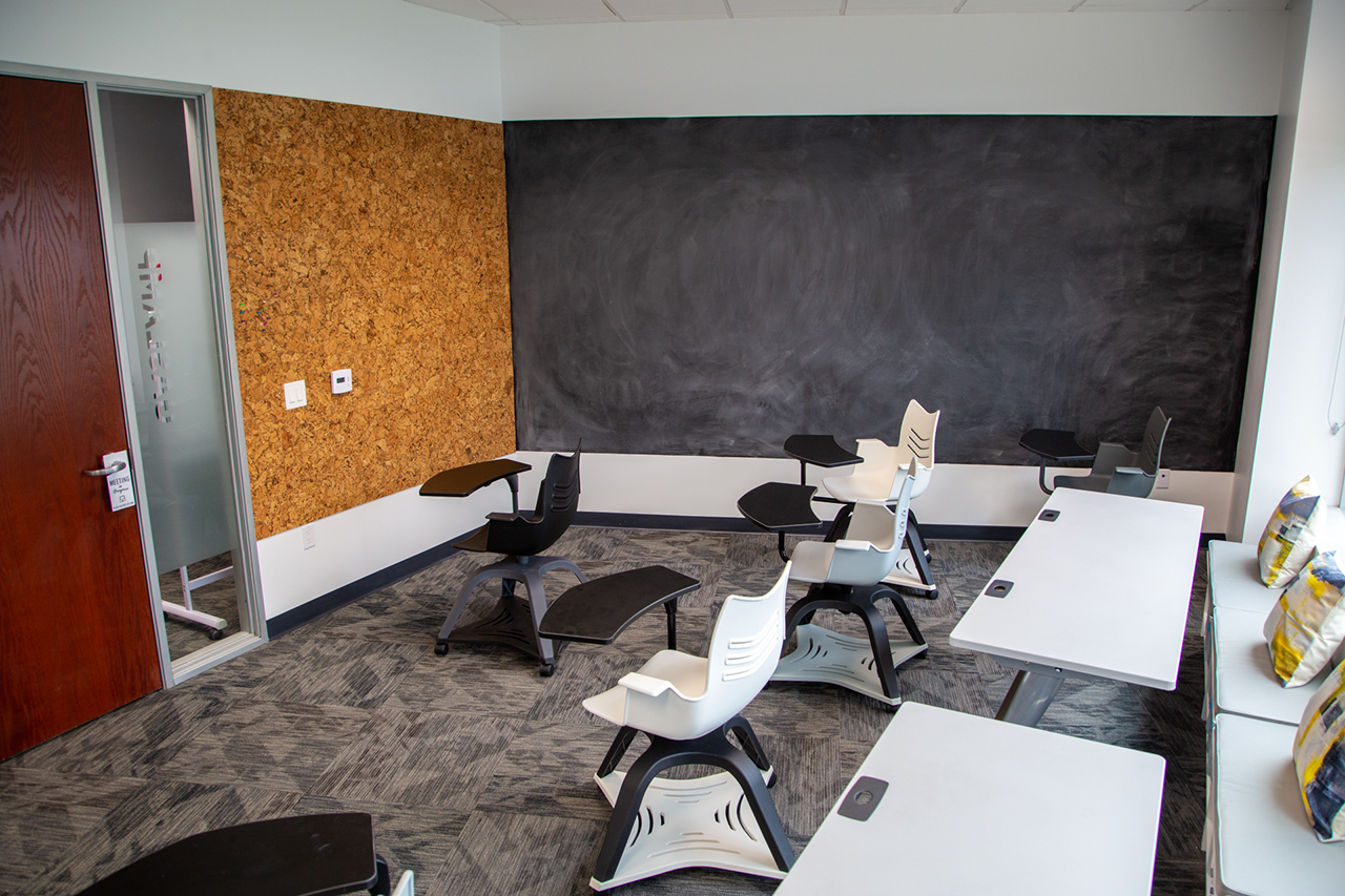 large room with classroom style rolling chairs, smaller tables, and chalkboard and cork board walls