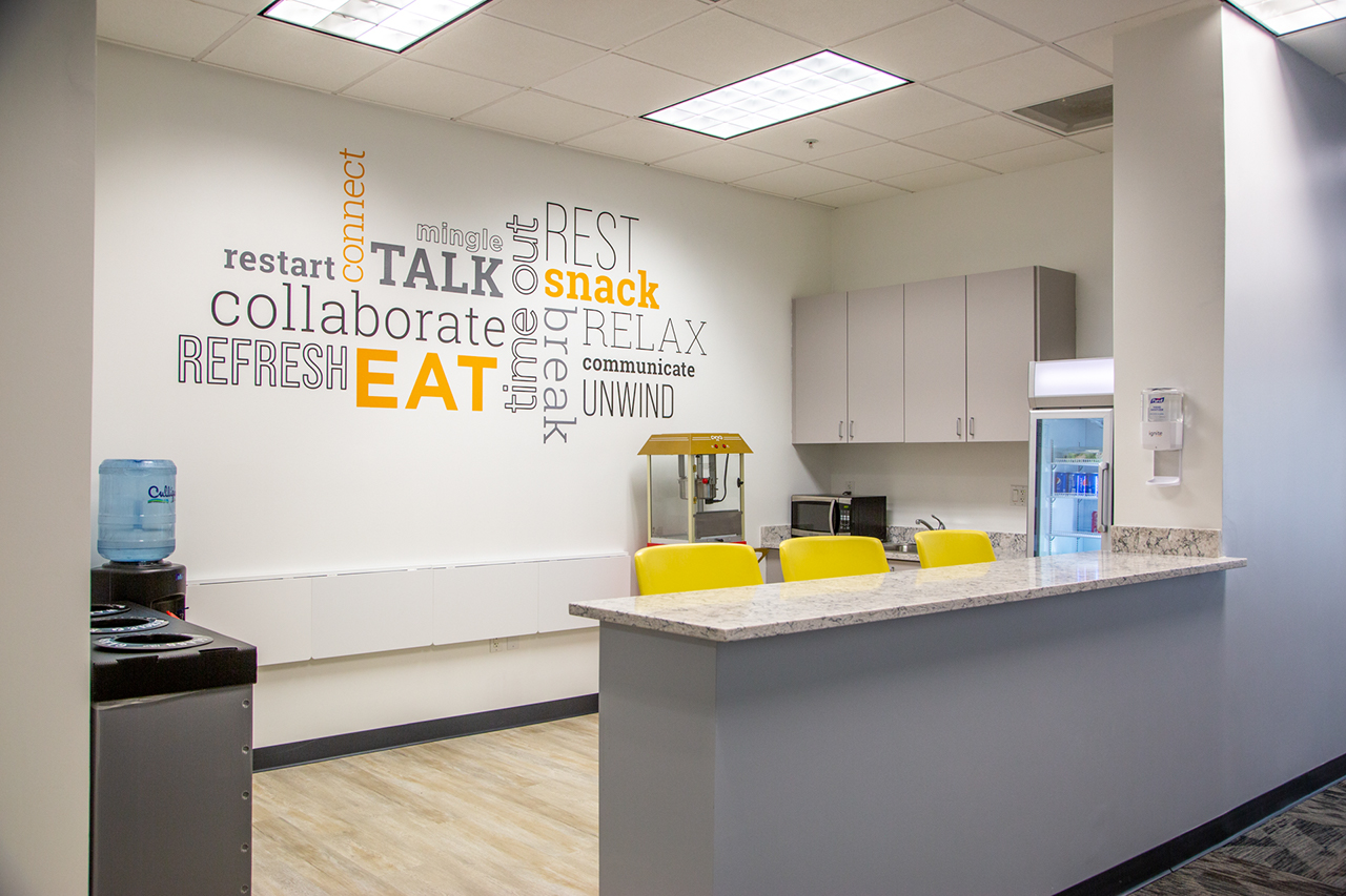 modern looking kitchen area with counter, cabinets, bar stools, refrigerator, and microwave