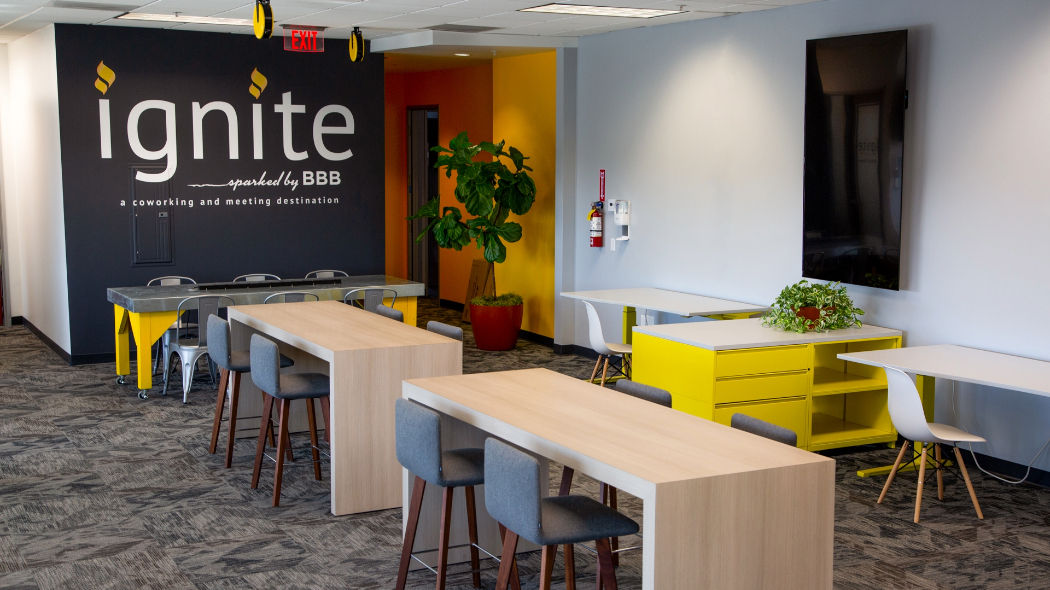 large room with modern furniture including tables, chairs, and cabinets with a large dark gray wall reading ignite sparked by BBB